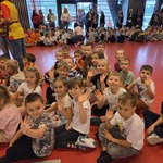 Dzieci siedzą na podłodze, machają rękami, wspólnie śpiewają Hymn Przedszkolaka.