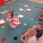 Na zdjęciu widzimy dzieci, które siedzą w rzędzie, a przed nimi dziewczynka, która trzyma godło Polski.