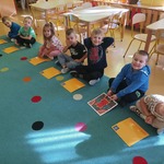 Na zdjęciu widzimy dzieci, które siedzą w rzędzie, a przed nimi leżą obrazki.