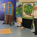 Aktor stoi na tle mapy Polski, obok leży kukiełka chłopca.