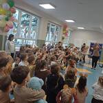 Na środku stoi nauczycielka i trzyma w górze uniesionego misia. Wokół niej stoją dzieci  i powtarzają ruchy nauczycielki.
