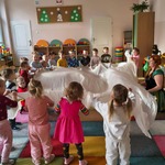 Dzieci i prowadząca trzymają materiał za krawędzie i machają nim w górę i w dół. 