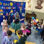 Nauczycielka prowadząca Bal Karnawałowy tańczy, a dookoła niej tańczą dzieci, które są przebrane w stroje karnawałowe.