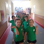 Na zdjęciu grupa dzieci w zielonych koszulkach. Przedszkolaki ustawione parami zwiedzają budynek szkoły.