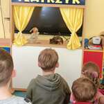 Dzieci siedzą na dywanie, przed nimi teatrzyk z kukiełkami.