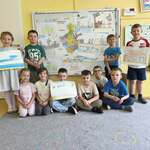 Grupa dzieci trzyma swoje prace z zabytkami Podlasia, za nimi tablica z mapą województwa podlaskiego.
