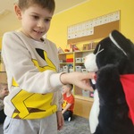 Chłopiec podaje rękę dla pluszowego czarno-białego kota z czerwoną peleryną.