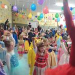 Duża sala z kolorowymi balonami, na której jest bardzo dużo uśmiechniętych, tańczących przedszkolaków. Z tyłu stoją cztery panie z podniesionymi rękoma. 