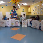 Dzieci trzymają przed sobą kartony z pokolorowanymi postaciami chłopca i dziewczynki. Za nimi cztery kobiety.