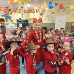 Na holu tańczą dzieci ubrane w różnokolorowe ubrania: czerwone, białe, zielone. Przedszkolaki na głowach mają kowbojskie kapelusze i kolorowe opaski.