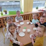 Sześcioro dzieci siedzi przy stoiku i je pączki