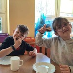 Zadowolone dzieci: dziewczynka w okularach i chłopiec siedzą przy stoliku i jedzą pączki.